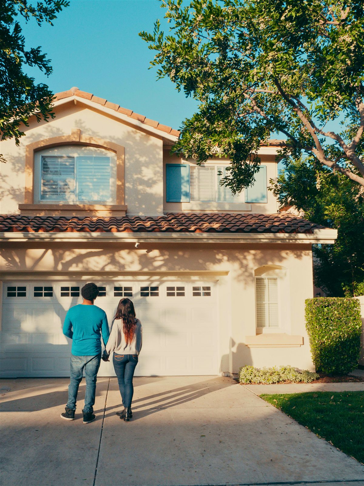 Homeowners standing in a driveway while reviewing the exterior of a house.